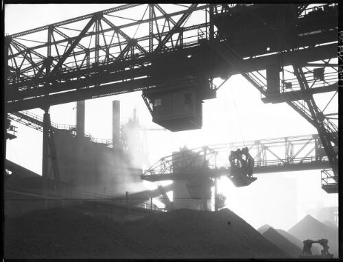 [Industry, piles of coal with overhead scaffolding, rigs, gantries, cranes and machinery, B.H.P. Steelworks] [picture] : [Newcastle, New South Wales] / [Frank Hurley]