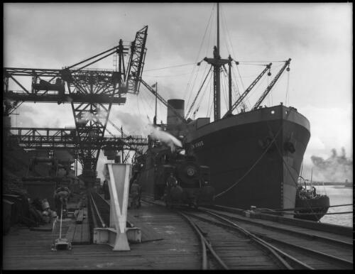 [The Iron Knob at Newcastle dock, with a steam engine and railway tracks, men, scaffolding, another ship and a crane] [picture] : [Newcastle, New South Wales] / [Frank Hurley]