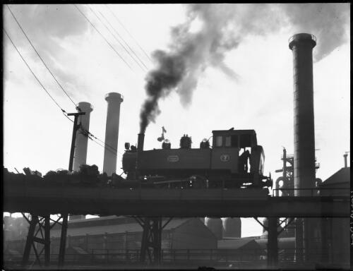 [A steam locomotive number 7 on an elevated railway track near three towers, B.H.P. Steelworks] [picture] : [Newcastle, New South Wales] / [Frank Hurley]