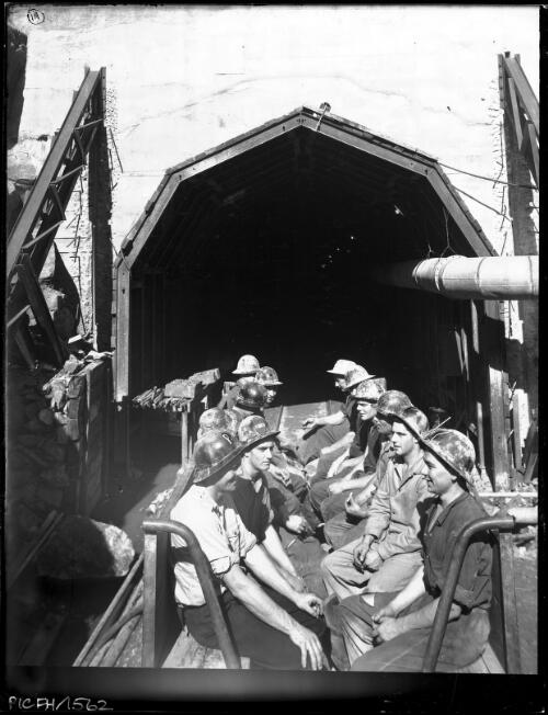 Tunnellers going on shift No.4 P. S. [men in underground tunnel on transport, power station, Kiewa, December 1947, 2] [picture] : [State Electricity Commission of Victoria] / [Frank Hurley]