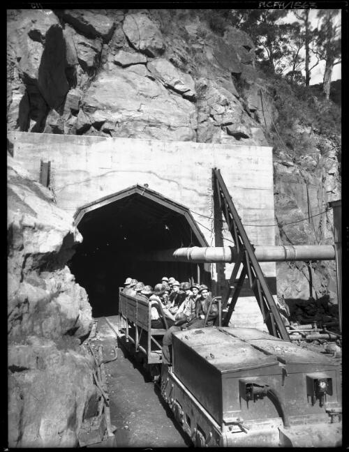 Tunnellers going on shift No.4 P. S. [men in underground tunnel on transport, power station, Kiewa, December 1947, 1] [picture] : [State Electricity Commission of Victoria] / [Frank Hurley]