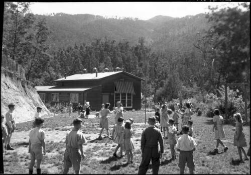 Bogong School [children playing in the yard in front of building, Kiewa, December 1947] [picture] : [State Electricity Commission of Victoria] / [Frank Hurley]