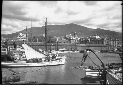 Docks looking to Mt Wellington, boat with sail half up [picture] : [Hobart, Tasmania] / [Frank Hurley]