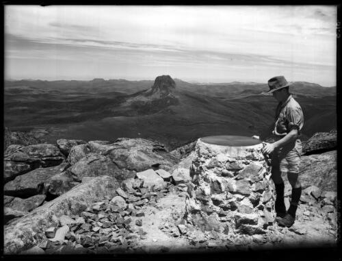 The Plate on the Pinnacle Cradle Mt [with figure in shorts and hat] [picture] : [Cradle Mountain, Tasmania] / [Frank Hurley]