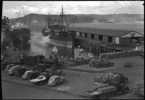 [CCS steam locomotive, ships Momba, Cape Corso, cars, trucks and Jones Pier, harbour] [picture] : [Tasmania] / [Frank Hurley]