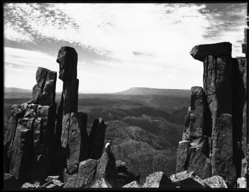 View of distant peaks framed in rocky formations [with figure] [picture] : [Cradle Mountain, Tasmania] / [Frank Hurley]