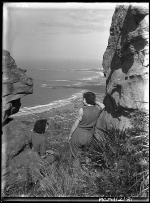Looking from cleft in rocks onto Sth Coast, Tony and Yvonne in FG [picture] : [South Coast, New South Wales] / [Frank Hurley]
