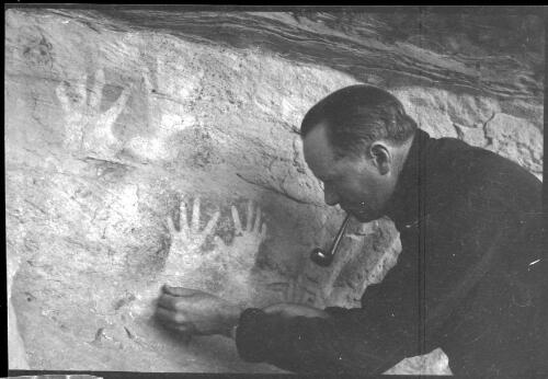 [Unidentified man with pipe in mouth, examining Aboriginal rock painting] [picture] / [Frank Hurley]