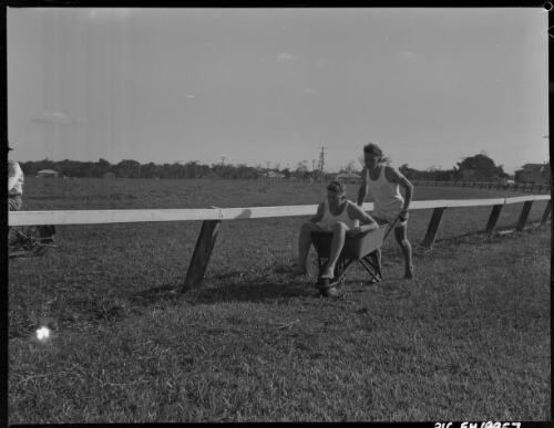 [Unidentified man pushing another man in a wheel  barrow] [picture] / [Frank Hurley]