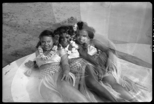 [Three women wearing leis and grass skirts, lying by the sea, 1] [picture] / [Frank Hurley]