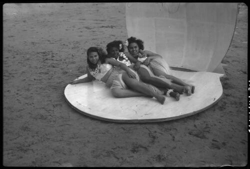 [Three women wearing leis and grass skirts, lying by the sea, 2] [picture] / [Frank Hurley]