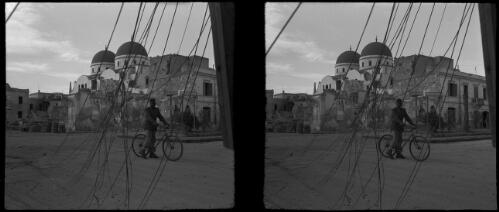 Scenes in Benghazi Cathedral  [felled telegraph wires and man with bike foreground, bombed town behind and then cathedral] [picture] : [Libya, World War II] / [Frank Hurley]