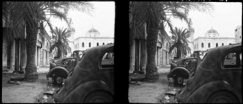 Scenes in town Hall Square, Benghazi [palm trees, burnt-out cars, mosque behind] [picture] : [Libya, World War II] / [Frank Hurley]