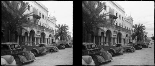 Scenes in town Hall Square, Benghaz [burnt out row of vehicles including cars, a tank and motorbike] [picture] : [Libya, World War II] / [Frank Hurley]