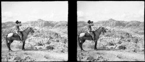[Soldier sitting on a horse, looking through binoculars in an arid, rocky terrain] [picture] / [Frank Hurley]