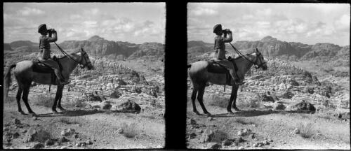 [Soldier sitting on a horse, looking through binoculars in an arid, rocky terrain] [picture] / [Frank Hurley]