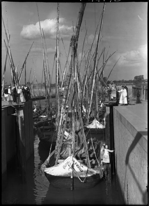 Feluccas entering a lock on the Ismalia Canal Egypt [boats crowded together at lock entrance, people watching from the top of the lock] [picture] : [Egypt, World War II] / [Frank Hurley]