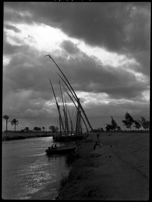 [Ismalia Canal, feluccas moored to canal bank, small boat and people on bank in foreground] [picture] : [Egypt, World War II] / [Frank Hurley]