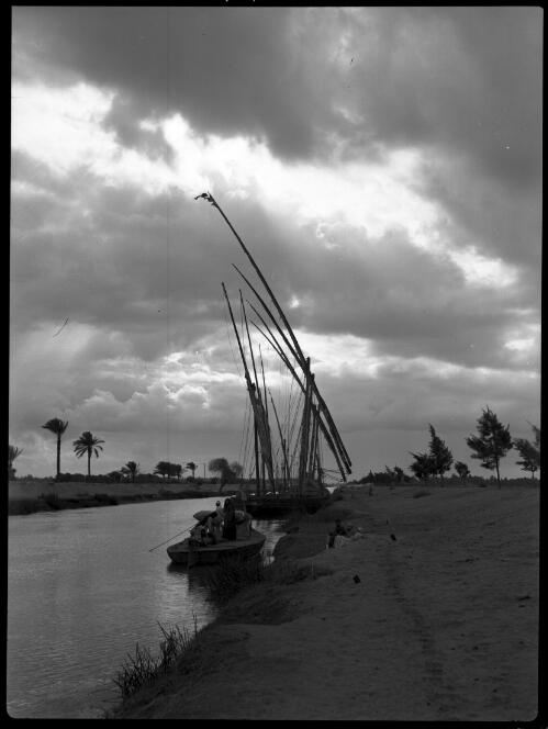 [Ismalia Canal, feluccas moored to canal bank, small boat in foreground with donkeys, produce and people,  small group resting on bank] [picture] : [Egypt, World War II] / [Frank Hurley]