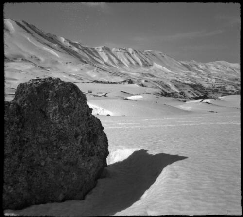 On the snow playground of the Lebanons, at the Cedars [boulder in the foreground, mountain slopes in the background] [picture] : [Lebanon, World War II] / [Frank Hurley]