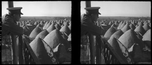 Nirab [man leaning on a balcony looking over adobe beehive houses] [picture] : [Syria, World War II] / [Frank Hurley]
