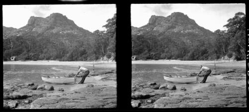 [Man pulling a boat out of the water in foreground, with distant cabin on left side and distant figure on the right in bush setting, ca. 1938-1947] [picture] : [Tasmania] / [Frank Hurley]
