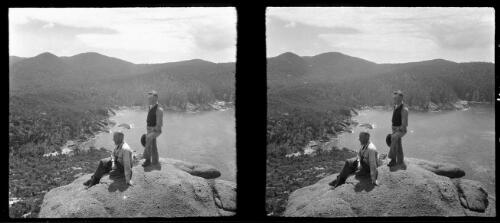[Two men on top of a rocky crag high above a waterway surrounded by distant hills, ca. 1938-1947] [picture] : [Tasmania] / [Frank Hurley]