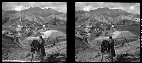 [Mount Lyell copper mine at Queenstown with a man standing next to large tripod mounted instrument, probably a camera, ca. 1938-1947] [picture] : [Queenstown, Tasmania] / [Frank Hurley]
