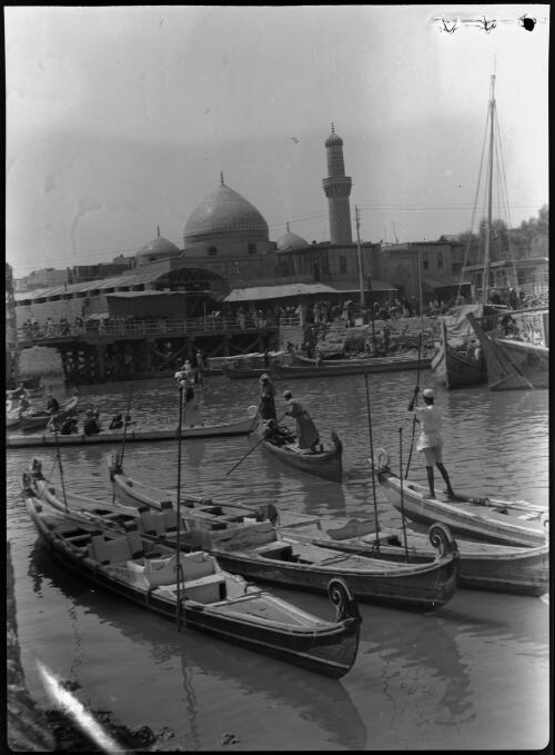 [Several canoes with curved prows and figures and poles in canal in front of a mosque, 1944] [picture] : [Iraq, World War II] / [Frank Hurley]