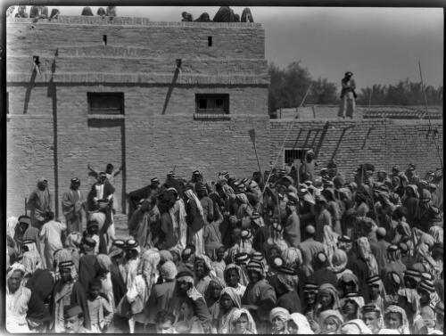 The natives indulge in a Hausa (Hosa) a stimulating dance, Chubaish [showing a large group of people and a building with a figure on the roof, 1944] [picture] : [Iraq, World War II] / [Frank Hurley]