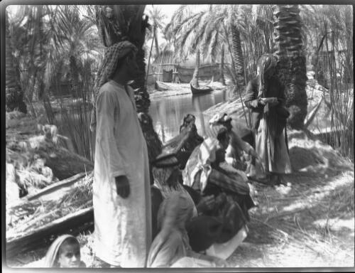 Typical beautiful glimpse at Chubaish [figures by the river under date palms, 1944] [picture] : [Iraq, World War II] / [Frank Hurley]
