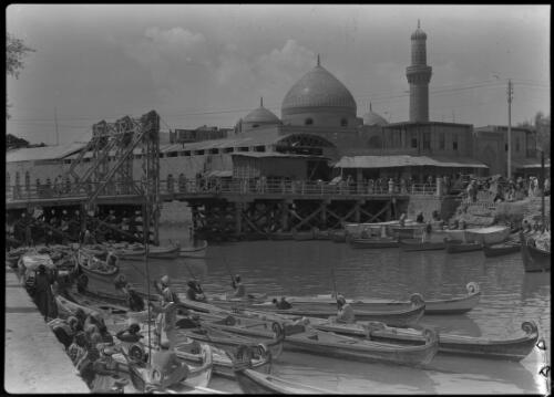 Basra [mosque with dome and minaret, canoes with curved prows, and a metal suspension bridge, 1944] [picture] : [Iraq, World War II] / [Frank Hurley]