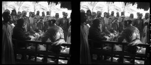 [Two men in military uniform sitting on benches with a large group of Arabs, 1944] [picture] : [Iraq, World War II] / [Frank Hurley]