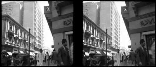 Glimpse Qasr El Nil Cairo [multi-storey buildings, street, figures, a car, a lamp post] [picture] : [Cairo, Egypt, World War II] / [Frank Hurley]