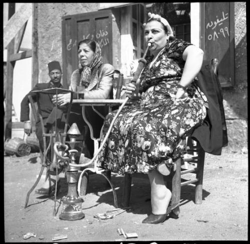 Village scenes shot at Misr studies on set [a woman smoking a large hookah with two other figures] [picture] : [Cairo, Egypt, World War II] / [Frank Hurley]