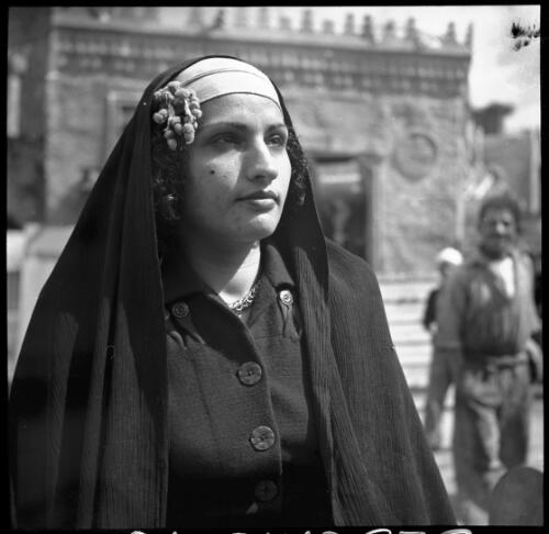 Village scenes shot at Misr studies on set [portrait of a woman wearing dark coloured top with buttons and a veil and headdress] [picture] : [Cairo, Egypt, World War II] / [Frank Hurley]