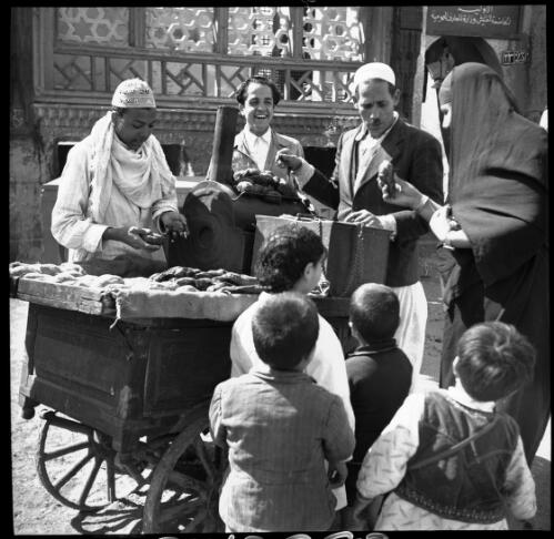 Village scenes shot at Misr, studies on set [figures of children and adults at a hand cart or barrow with food, 2] [picture] : [Cairo, Egypt, World War II] / [Frank Hurley]