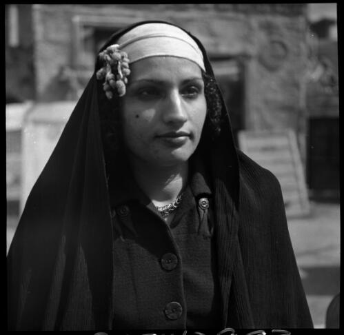 Village scenes shot at Misr, studies on set [portrait of a woman wearing a dark coloured top with buttons and a veil and headdress] [picture] : [Cairo, Egypt, World War II] / [Frank Hurley]