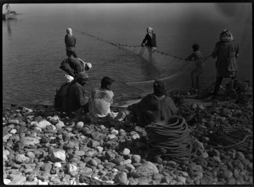 Fishermen, Sea of Galilee [figures standing in the water and sitting on shore with ropes and nets] [picture] : [Galilee, World War II] / [Frank Hurley]
