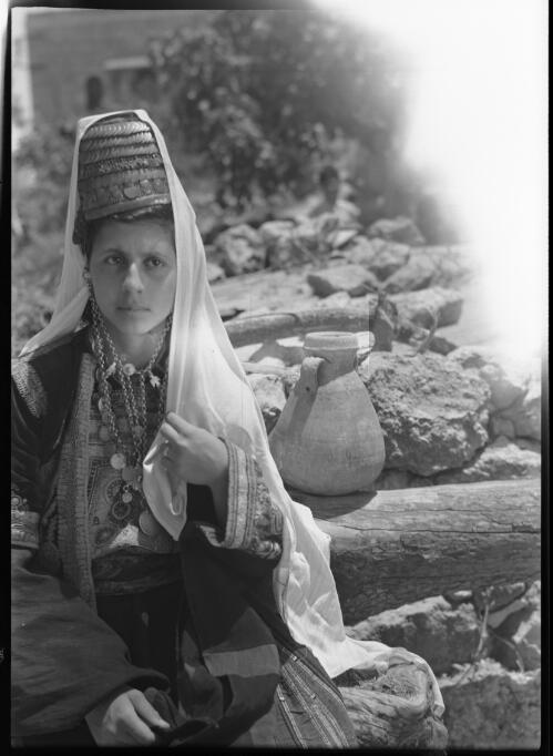 Girl from Beit Jala near Bethlehem wearing the characteristic headdress of the Aria [full face with vessel or urn in background, Palestine] [picture] : [Portrait Studies, Libya, World War II] / [Frank Hurley]