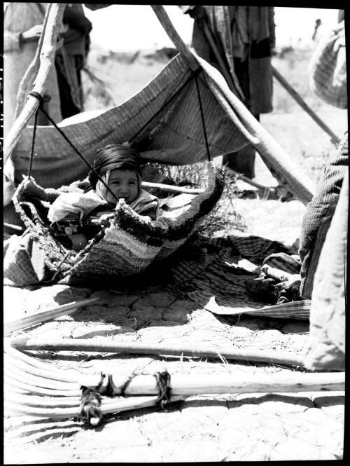 [Infant in a cradle in a tent, with other figures in the background] [picture] : [Portrait Studies, Libya, World War II] / [Frank Hurley]