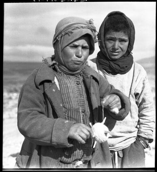 [Two figures with headdresses, one holding a small hand-held device for spinning wool] [picture] : [Portrait Studies, Libya, World War II] / [Frank Hurley]