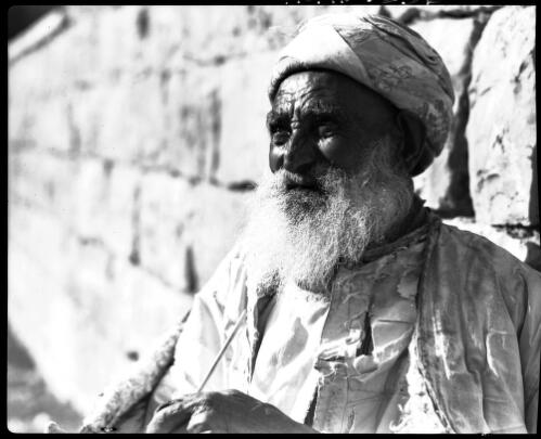 [Elderly figure wearing a headdress and leaning against the Wailing Wall?] [picture] : [Portrait Studies, Libya, World War II] / [Frank Hurley]