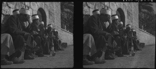 [A group of seated men wearing hats relax by a lane, smoking a pipe] [picture] / [Frank Hurley]