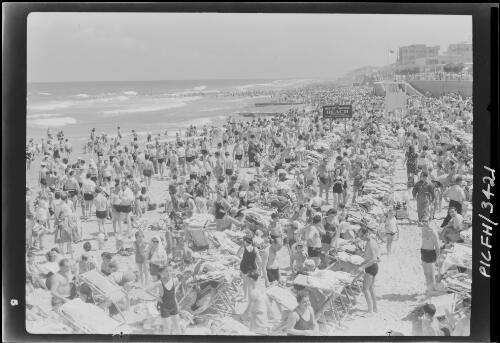 Tel Aviv [crowded beach with deck chairs, life guard tower, and sign 'WD Military Bathing Beach by order of Military Commander'] [picture] / [Frank Hurley]