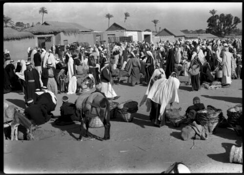 Esdud Fair [stacked baskets, donkeys, and seated men in foreground] [picture] / [Frank Hurley]