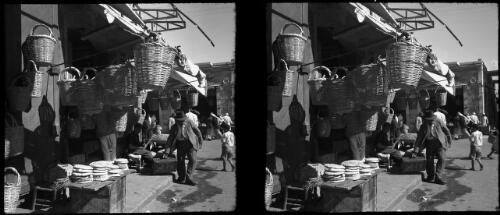 Jaffa [market scene, man picking up suitcase, hanging baskets and stacks of bread?] [picture] / [Frank Hurley]
