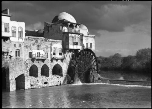 [Picturesque scene of riverside town buildings, waterwheel and weir, Hama] [picture] : [Syria, World War II] / [Frank Hurley]