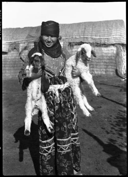 Mainly sheep scenes around Bedouin Camp in Northern Syria [smiling Bedouin woman with two lambs in arms] [picture] / [Frank Hurley]