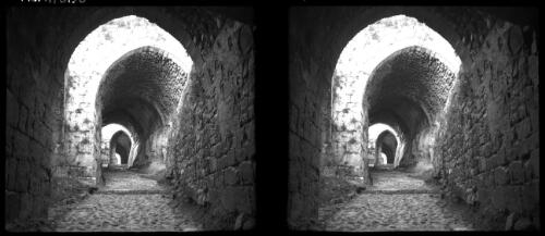 The Crac-de-Chevalier, one of the finest preserved of the Crusader fortresses in N. Syria [view through a dark stone passageway] [picture] / [Frank Hurley]